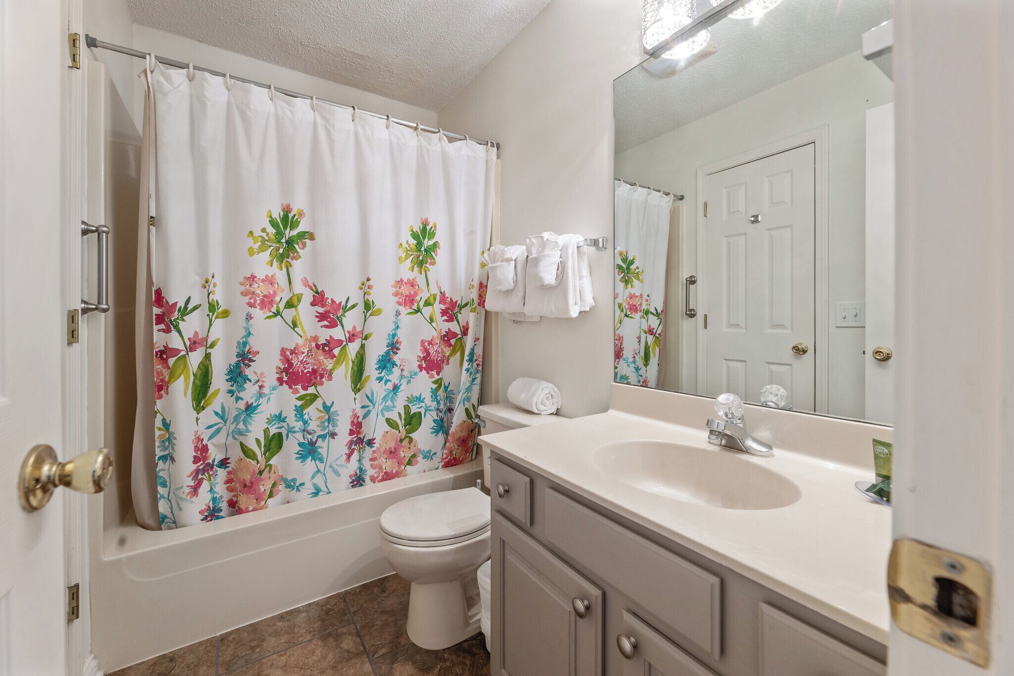 A bathroom with a toilet, a sink, a mirror, and a shower curtain with floral patterns.