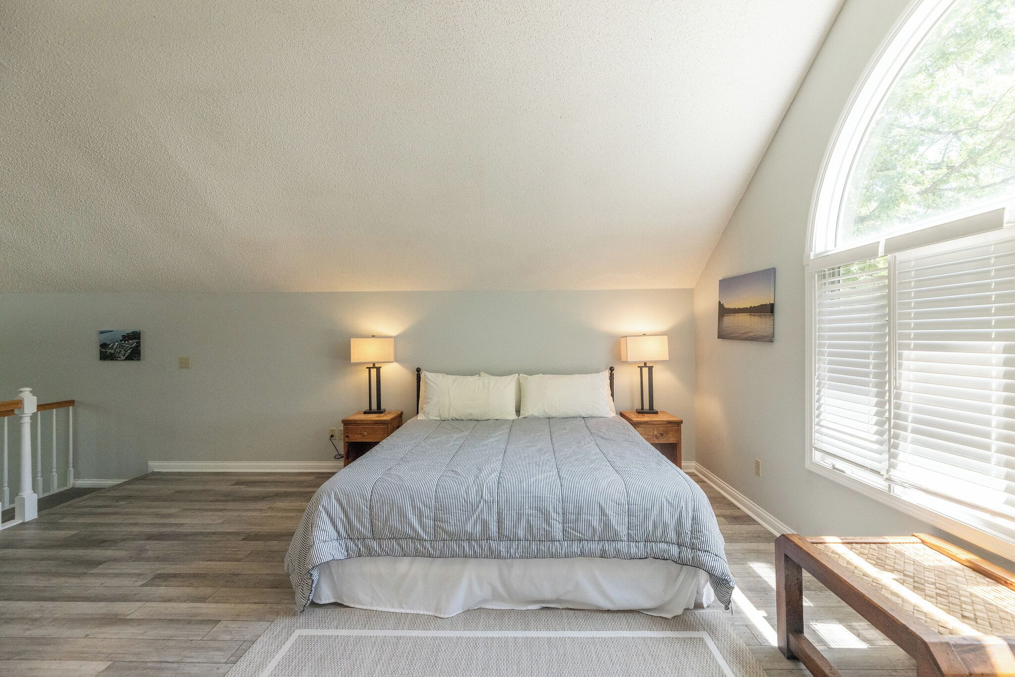 Un dormitorio con cama, dos lámparas de noche, ventana con persianas y vistas al exterior.