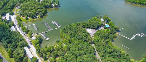 An aerial view of a lakeside property with a marina, parking area, and buildings surrounded by dense greenery.
