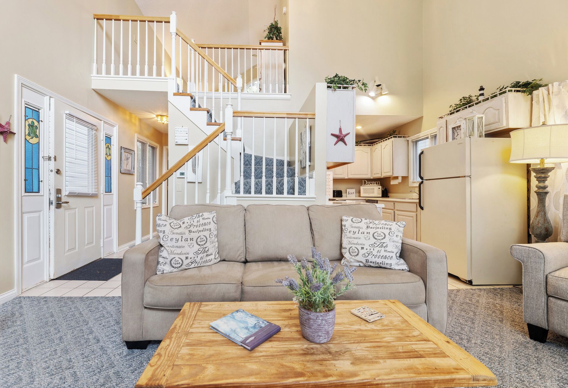A living room with a beige sofa, a coffee table, and a staircase with white railings.