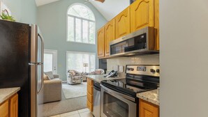 A modern kitchen with stainless steel appliances, wooden cabinets, and a large window providing natural light. - Two Bedroom Bayside Condo (Grand Rivers)