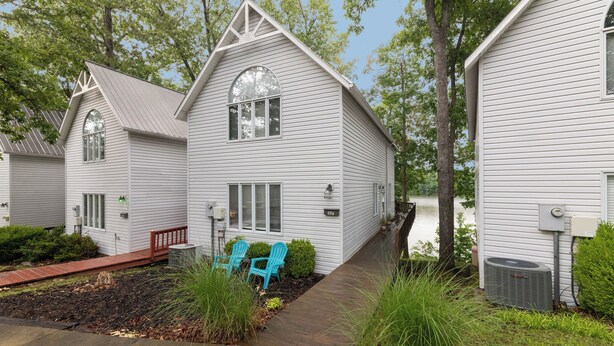 A white cabin-style house with a large window, a porch, and a small deck. - Two Bedroom Bayside Condo (Grand Rivers)