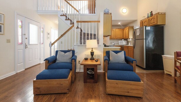 Amplia sala de estar con una escalera de madera, una cocina con armarios de madera y dos sillones azules.