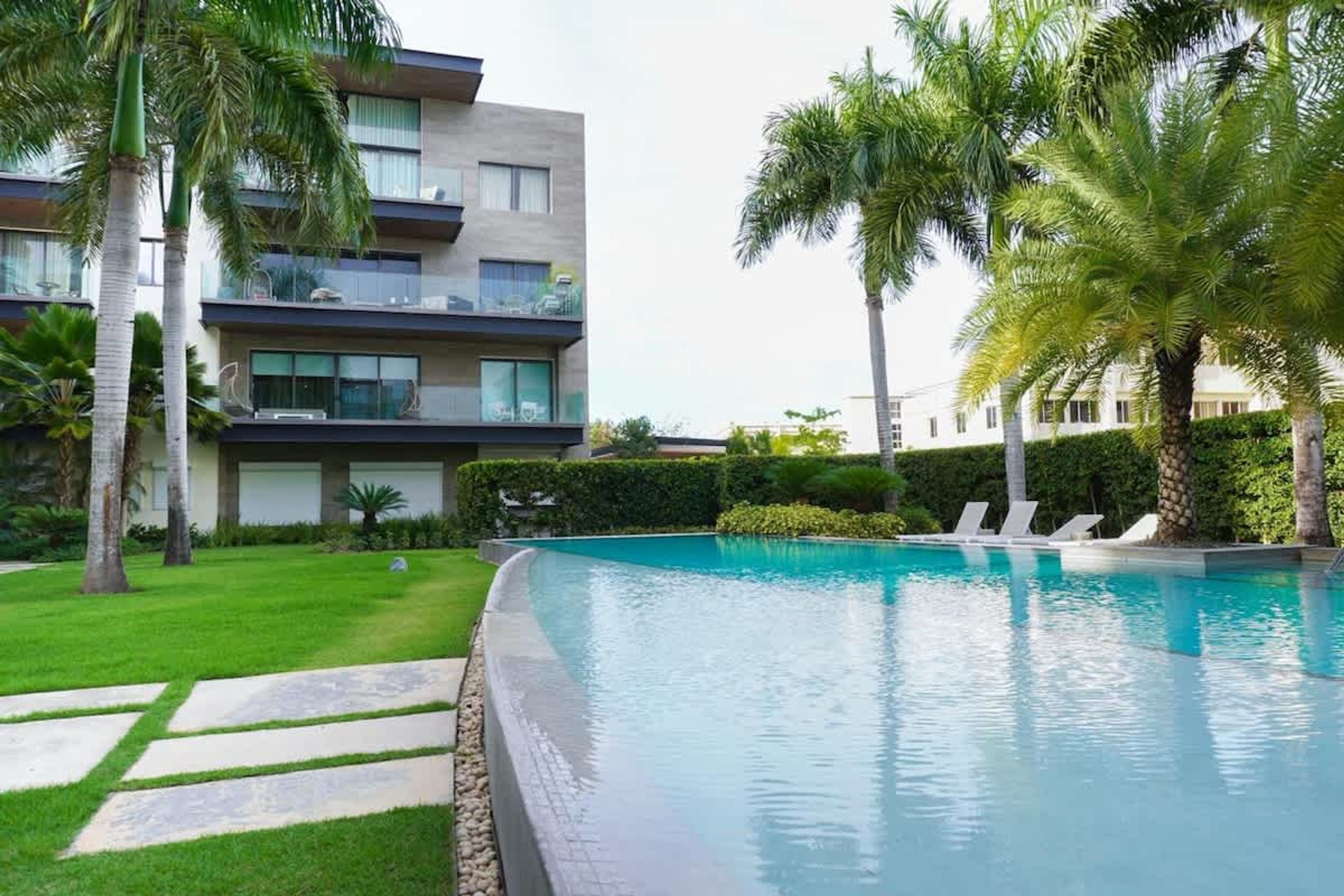 Um hotel moderno com piscina, palmeiras e um gramado bem cuidado.