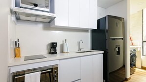 A modern kitchen with white cabinets, a built-in oven, a microwave, a coffee maker, and a refrigerator. - Perfect 1 BR in Centro Historico (Bogotá)