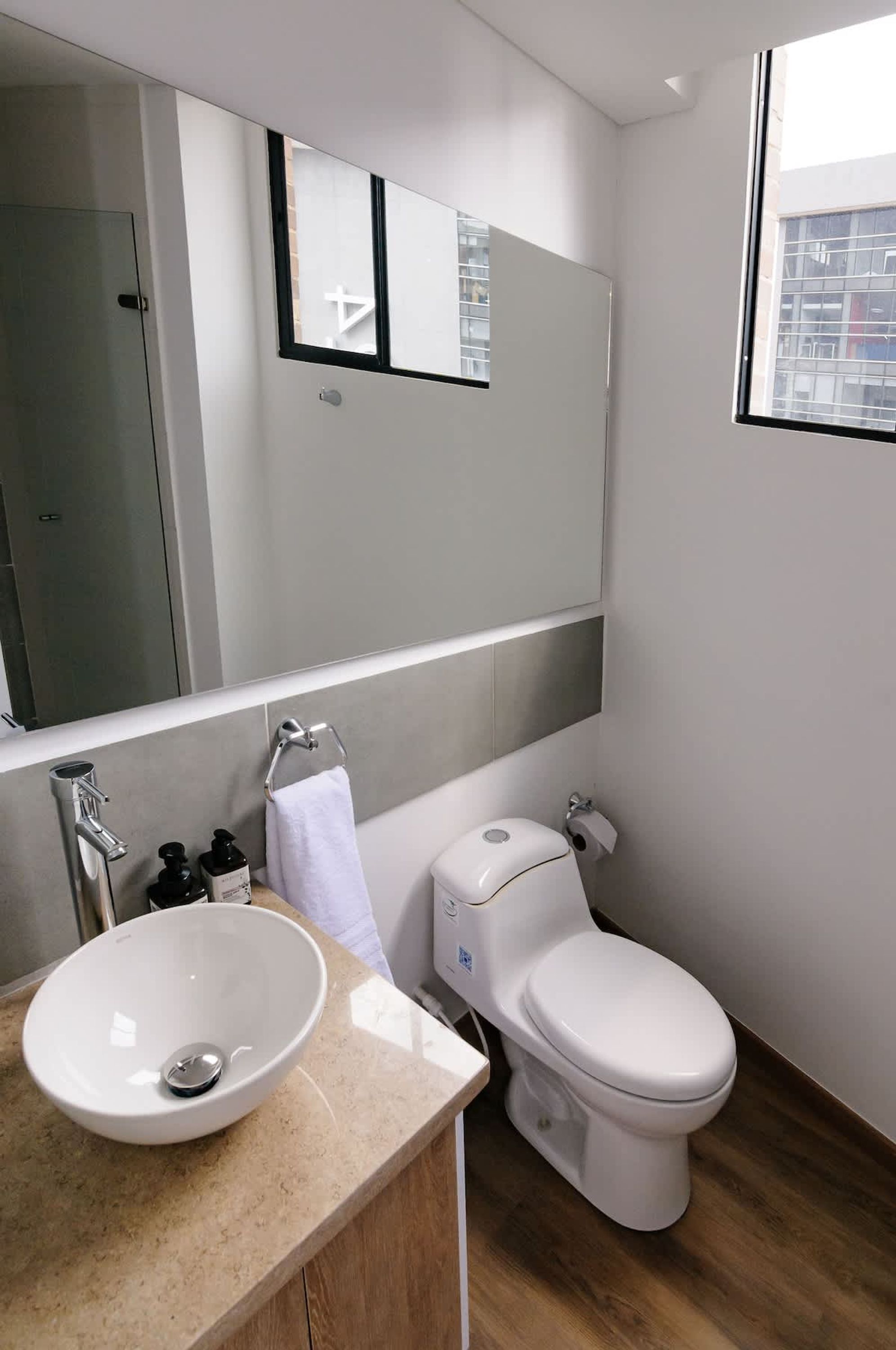 Ein modernes Badezimmer mit einem weißen Waschbecken, einer Toilette und einem großen Spiegel über dem Waschbecken.