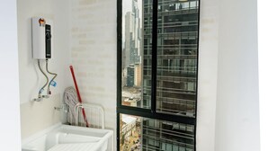 A laundry area with a washing machine, a water heater, and a window with a city view. - Perfect 1 BR in Centro Historico (Bogotá)