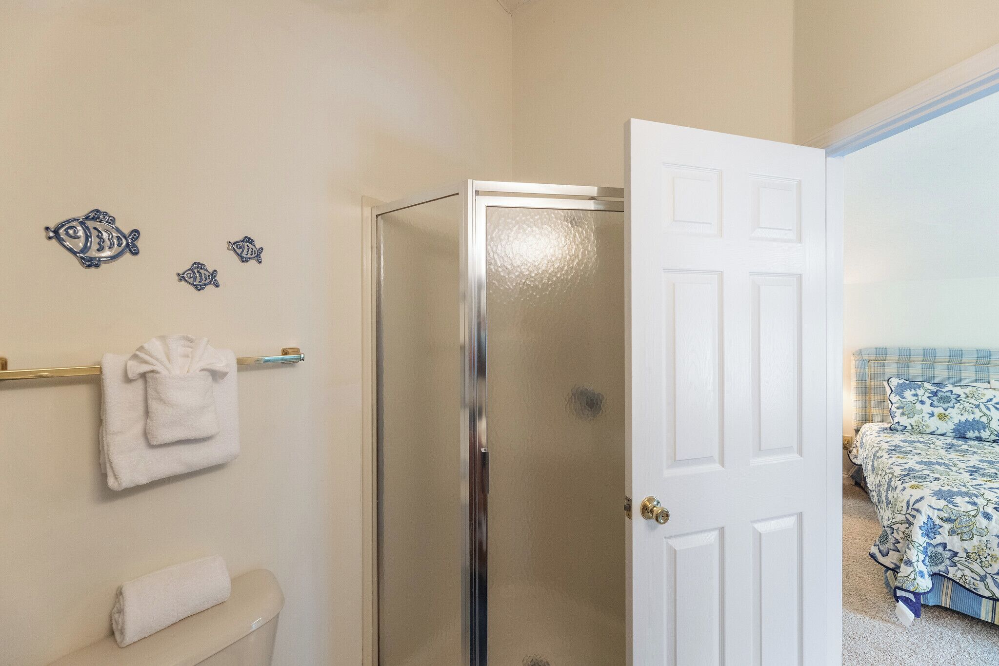 A bathroom with a toilet, a towel rack with towels, and a glass shower enclosure.