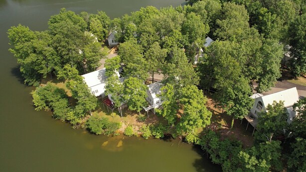 An aerial view of a lakeside property with several houses surrounded by dense greenery and trees. - Two Bedroom Bayside Condo (Grand Rivers)