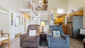 A living room with two armchairs, a lamp, and a staircase leading to a second floor. - Two Bedroom Bayside Condo (Grand Rivers)