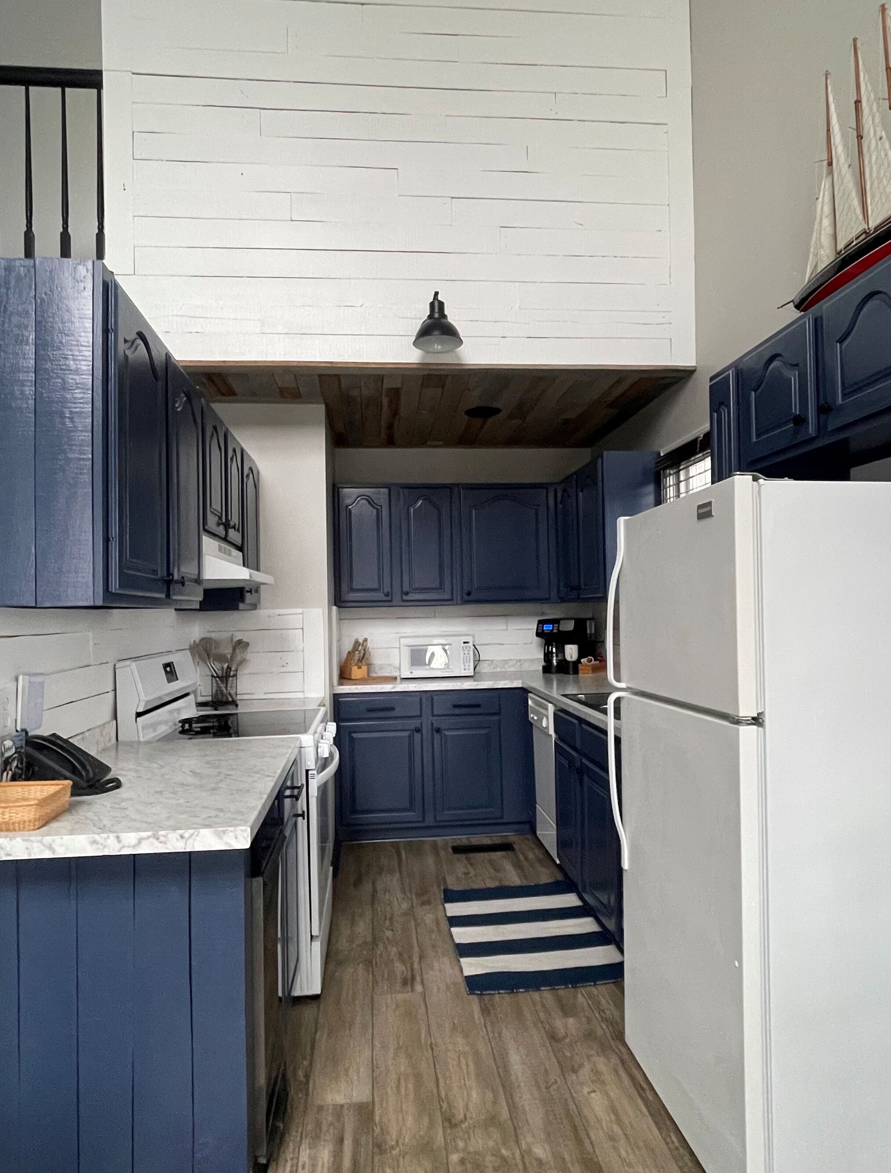 A narrow kitchen with dark blue cabinets, a white refrigerator, and a wooden floor.