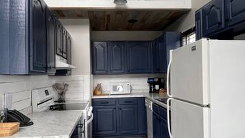 A narrow kitchen with dark blue cabinets, a white refrigerator, and a wooden floor.