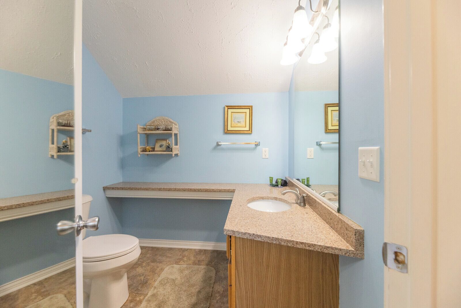 A bathroom with a toilet, sink, and bathtub. There are two shelves with decorative items and a mirror above the sink.