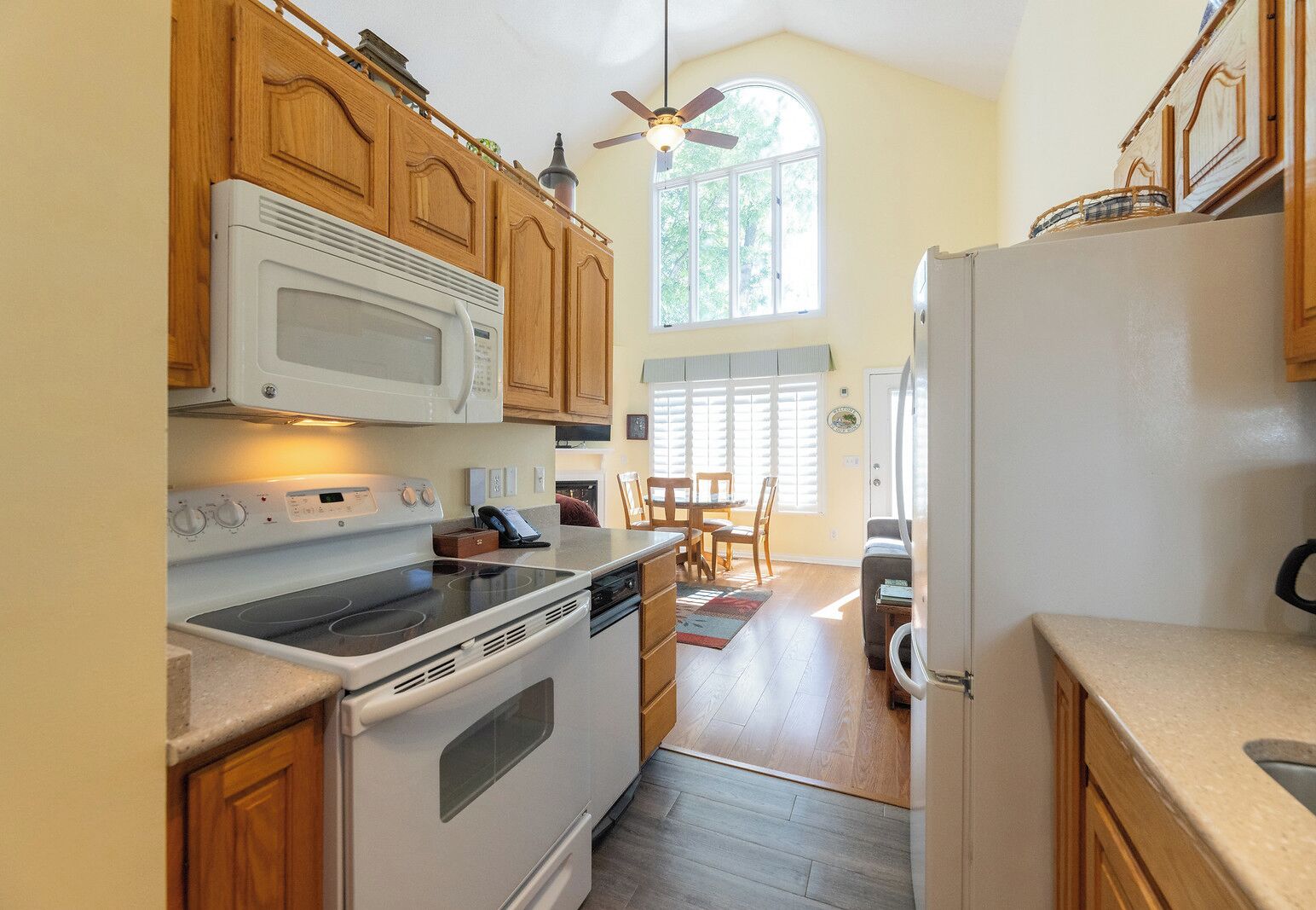 A kitchen with wooden cabinets, a microwave, a stove, and a refrigerator. There is a dining area with a table and chairs.