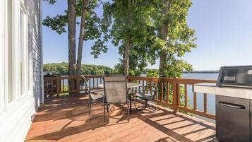Une terrasse en bois avec un barbecue, des chaises et une table, le tout donnant sur un lac.