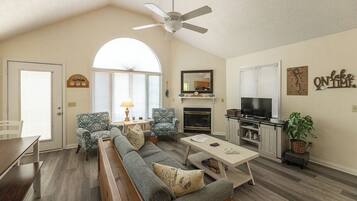 A spacious living room with a high ceiling, a fireplace, a television, and a dining area with a bench.