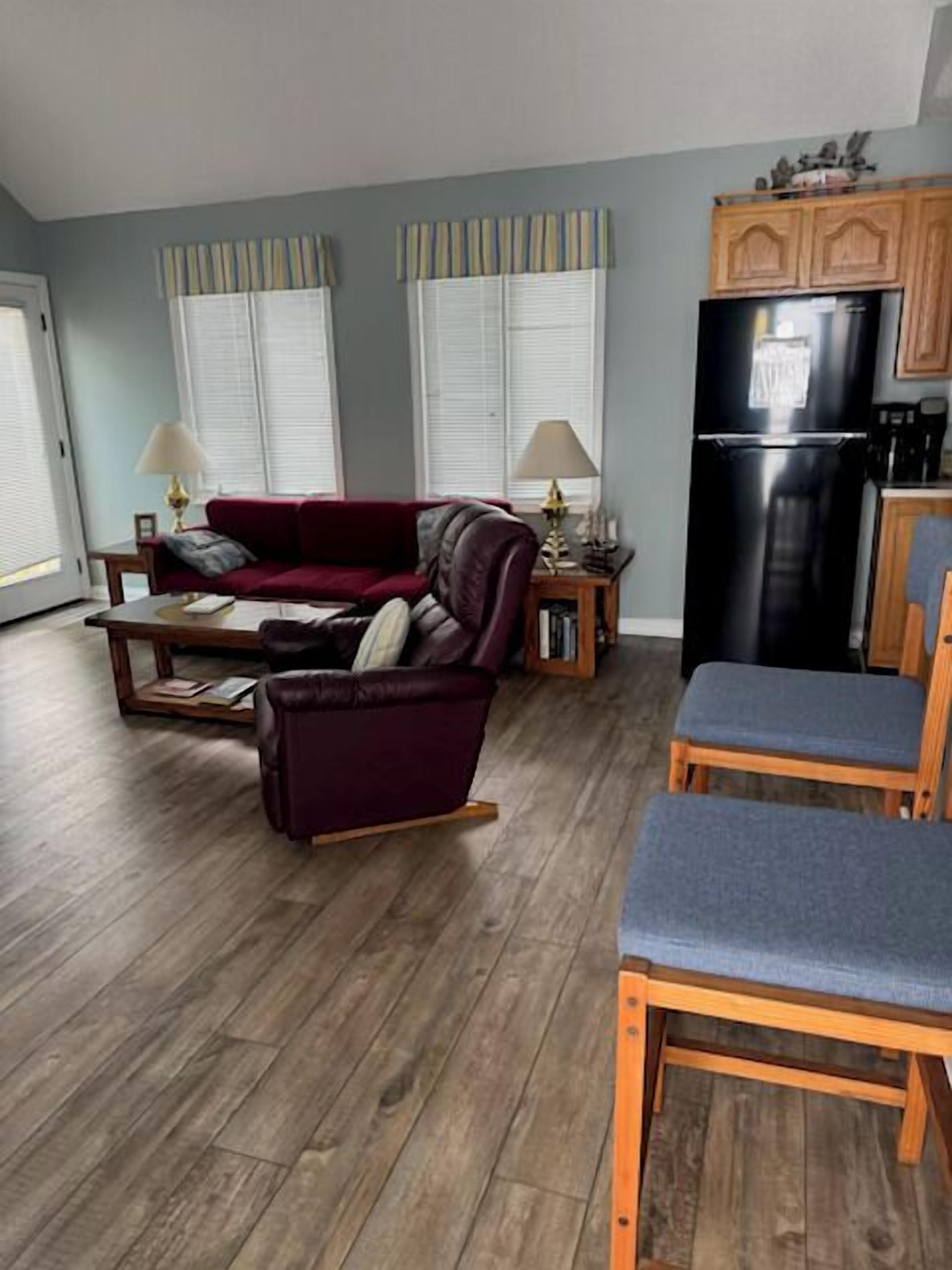 A living room with a sofa, chairs, a dining table, and a kitchen area with a refrigerator.