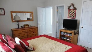 A bedroom with a large bed, a dresser, a television on a stand, and a door leading to another room. - One Bedroom Bayside Condo (Grand Rivers)