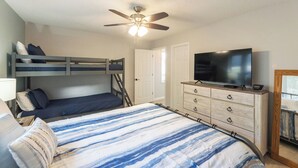 A bedroom with bunk beds, a ceiling fan, a TV, and a dresser.