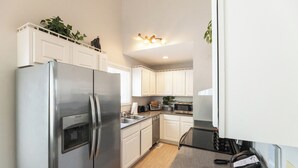 A compact kitchen with white cabinets, a stainless steel refrigerator, a microwave, and a sink.