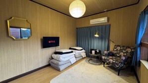 A hotel room with a bed, a chair, a TV displaying 'NETFLIX', a mirror, and an air conditioning unit.