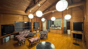 A wooden cabin interior with a dining area, sofas, a round table, and a kitchen area with a refrigerator and a television.