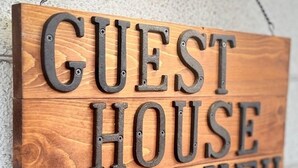 A wooden sign with the words "GUEST HOUSE YUFU" mounted on a wall.