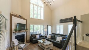 A spacious living room with a fireplace, a television, and a staircase. - Two Bedroom Bayside Condo (Grand Rivers)