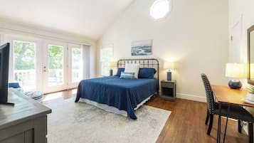 Ein Schlafzimmer mit einem großen Bett, einem Schreibtisch mit Stuhl, einem Fernseher und Blick auf einen Balkon.