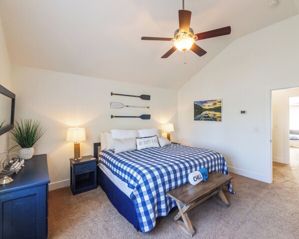 A bedroom with a bed, a ceiling fan, a nightstand, a lamp, a bench, a wall-mounted paddleboard, and a painting. - Four Bedroom Yacht Condo (Grand Rivers)