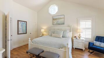 A bedroom with a large bed, a nightstand, a bench, a blue chair, and a window with blinds.