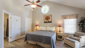 A bedroom with a bed, two bedside tables, a chair, a ceiling fan, a window with blinds, and a painting on the wall. - Four Bedroom Yacht Condo (Grand Rivers)