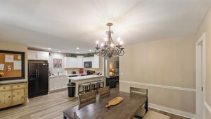 A spacious dining area with a wooden table and benches, a kitchen with white cabinets and a black refrigerator, and a chandelier. - Four Bedroom Yacht Condo (Grand Rivers)