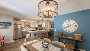 A modern kitchen with a stainless steel refrigerator, a dining area with a table and chairs, and a clock on the wall. - Four Bedroom Yacht Condo (Grand Rivers)