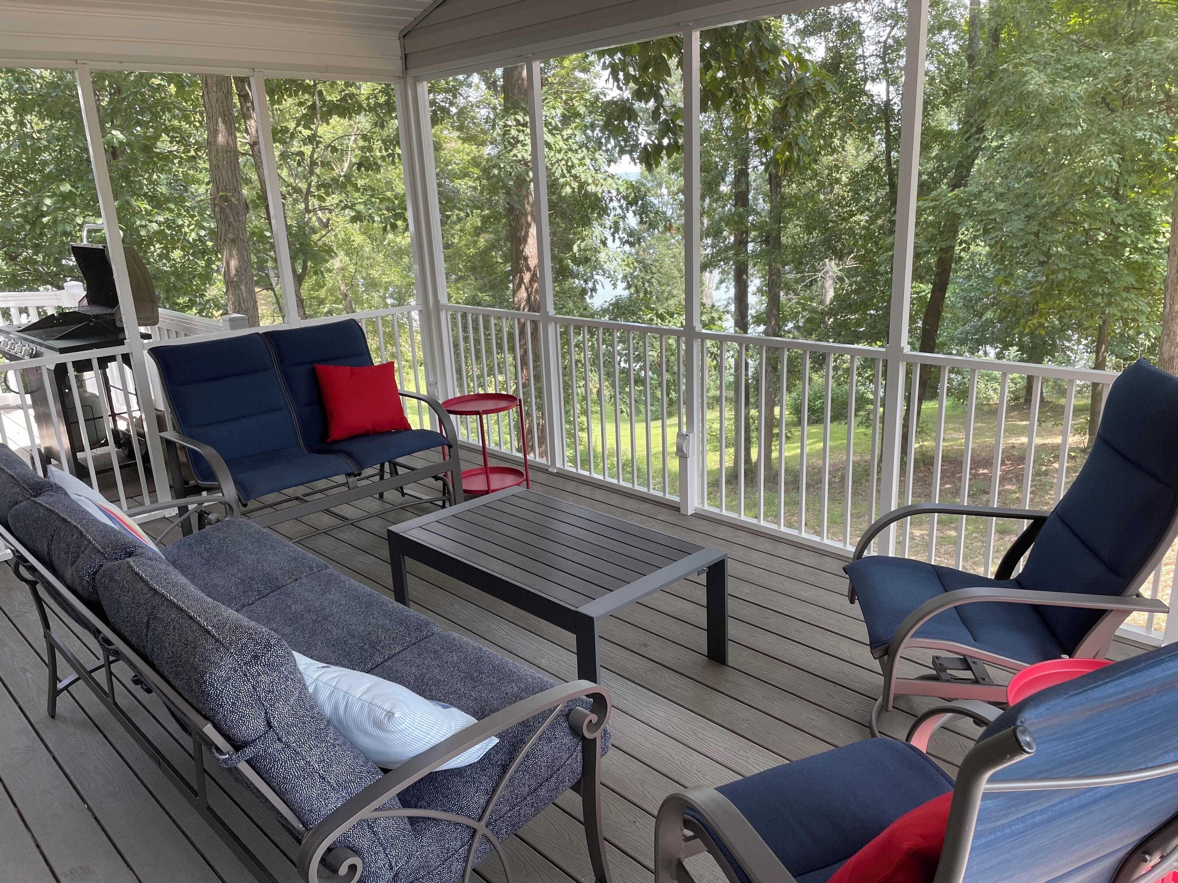En overdækket terrasse med siddepladser, et lille bord og en grill.
