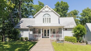 A white two-story house with a front porch, a central arched window, and a small garden area. - Four Bedroom Yacht Condo (Grand Rivers)