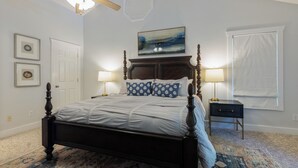 A bedroom with a large bed, a ceiling fan, a window with blinds, and a nightstand with a lamp. - Four Bedroom Yacht Condo (Grand Rivers)