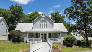 A two-story house with a front porch, a small staircase leading to the entrance, and a well-maintained lawn. - Four Bedroom Yacht Condo (Grand Rivers)