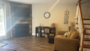 A living room with a fireplace, a sofa, a bookshelf, and a staircase. - Four Bedroom Yacht Condo (Grand Rivers)