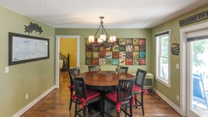 Un comedor con una mesa redonda de madera rodeada por seis sillas con cojines rojos, una araña y una pared decorada con varias obras de arte enmarcadas.