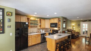 Una cocina moderna con armarios de madera, un refrigerador negro, un microondas y una isla grande con taburetes de bar.