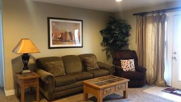 A living room with a sofa, a coffee table, a lamp, a chair, a plant, and a door.