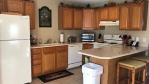 Une cuisine avec des meubles de rangement en bois, un réfrigérateur, un four à micro-ondes, une cuisinière et une poubelle.