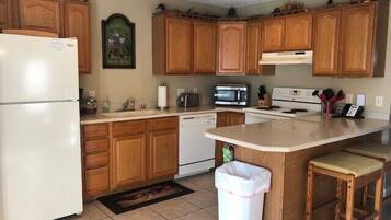 A kitchen with wooden cabinets, a refrigerator, a microwave, a stove, and a trash can.