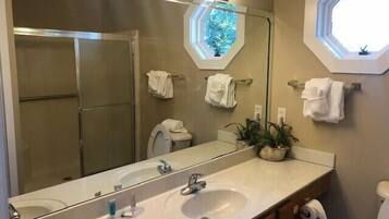 Un baño con dos lavamanos, un espejo grande y una ducha. Hay toallas colgadas en la pared y una planta en maceta sobre el mostrador.