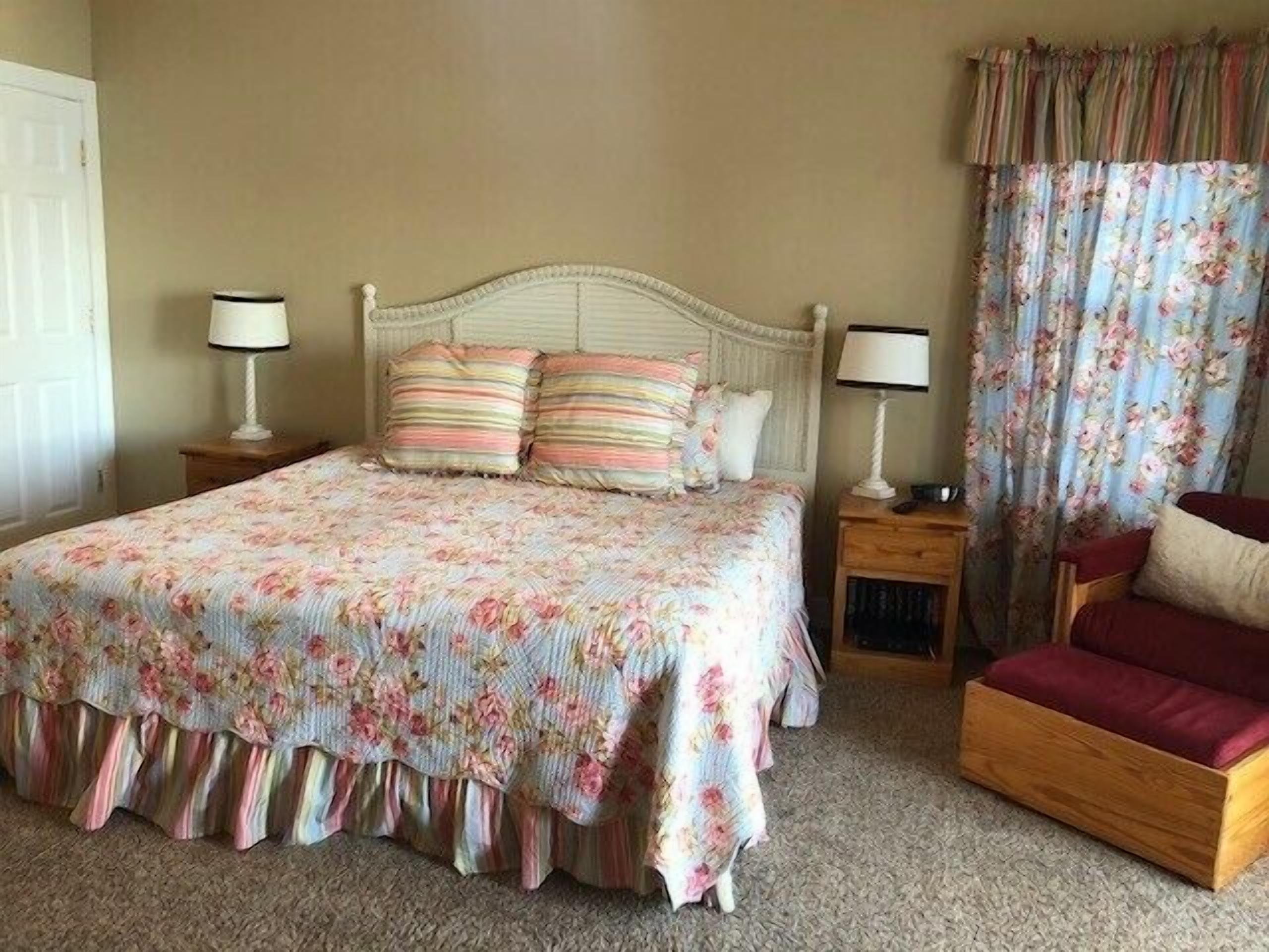Una camera da letto con un letto, due comodini, una sedia e una finestra con tende.