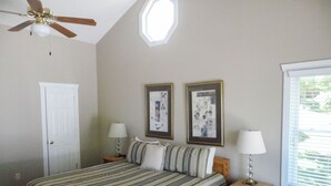 Ein Schlafzimmer mit einem Bett, zwei Nachttischen, einem Deckenventilator, einer Tür und zwei gerahmten Bildern an der Wand.