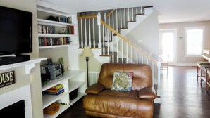 Ein Wohnzimmer mit einem braunen Ledersofa, einem Fernseher und einem Bücherregal.