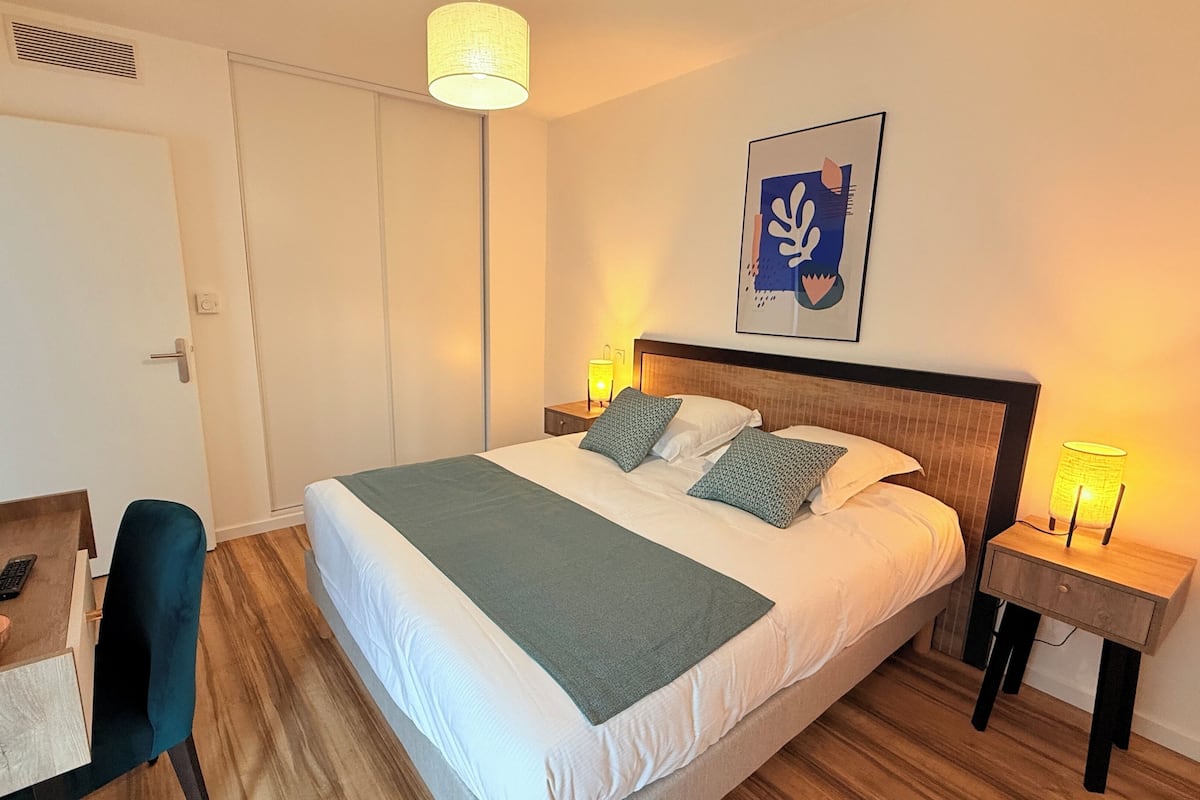 A neatly arranged hotel room with a bed, bedside tables, a desk with a chair, and a television.