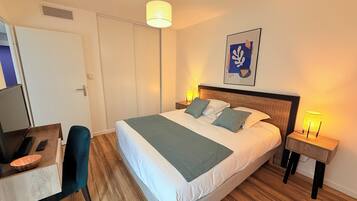 A neatly arranged hotel room with a bed, bedside tables, a desk with a chair, and a television.